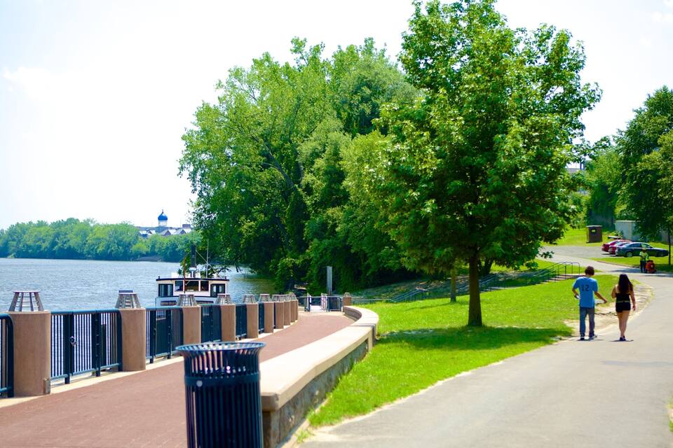 A riverside walkway with a boat dock, trees, and a distant building with a dome.
