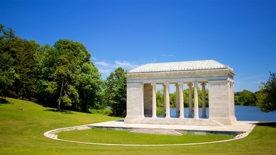 A neoclassical pavilion with columns, surrounded by a well-manicured lawn and a body of water.