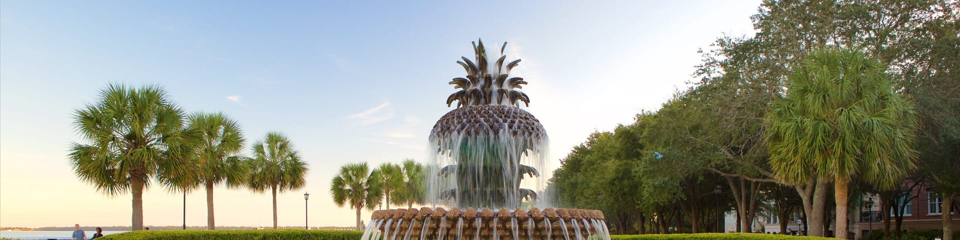 A tiered water fountain surrounded by manicured hedges and palm trees.