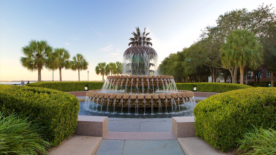 A tiered water fountain surrounded by manicured hedges and palm trees.
