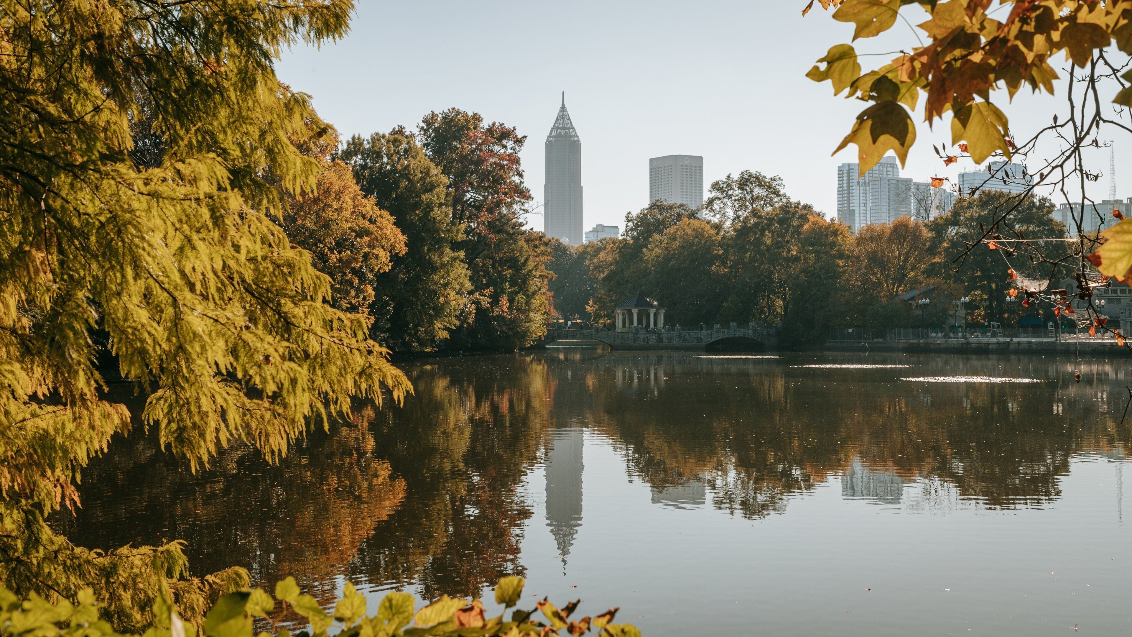 A calm lake with autumn foliage, a traditional pavilion, and a modern skyscraper in the background.