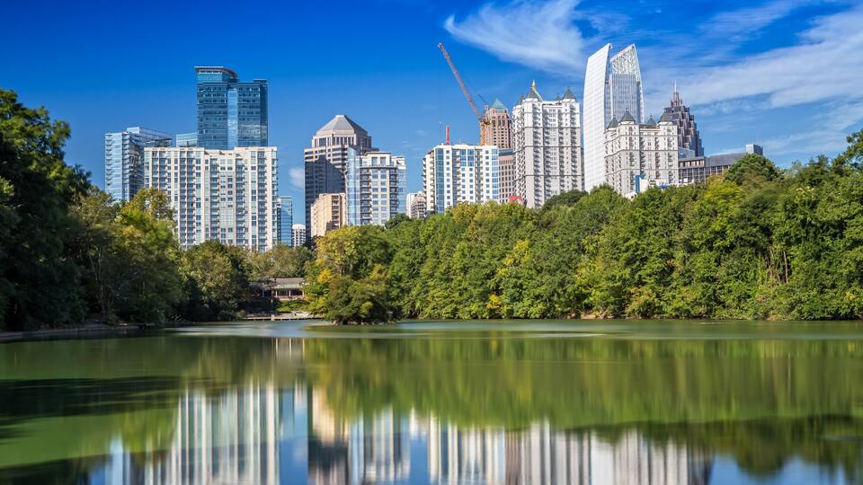 Un horizonte urbano con edificios altos, un lago tranquilo y un bosque denso en primer plano.