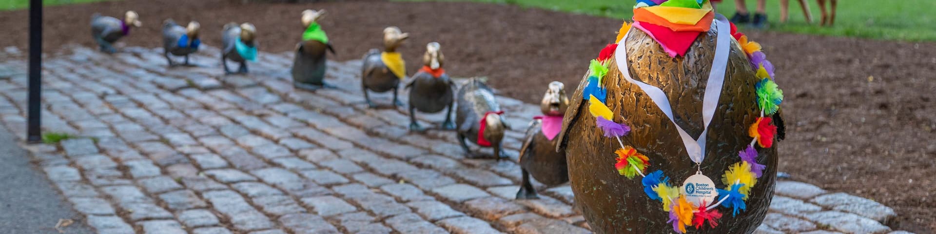 A row of bronze sculptures of birds with colorful decorations on a cobblestone path in a park.