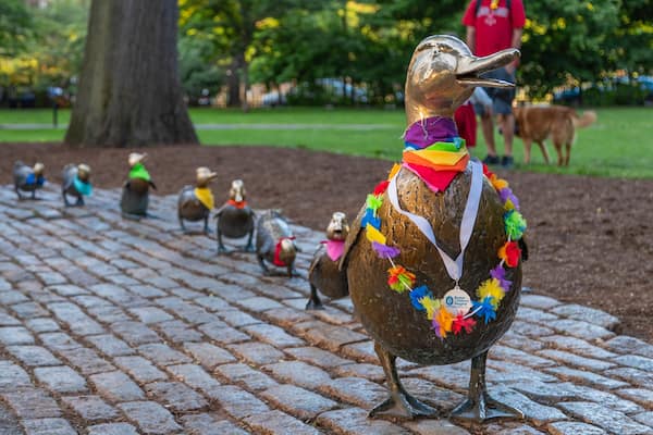 Fileira de esculturas de bronze de pássaros com decorações coloridas, em um caminho de paralelepípedos em um parque.