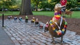Een rij bronzen beeldjes van vogels met kleurrijke decoraties langs een geplaveid pad in een park.