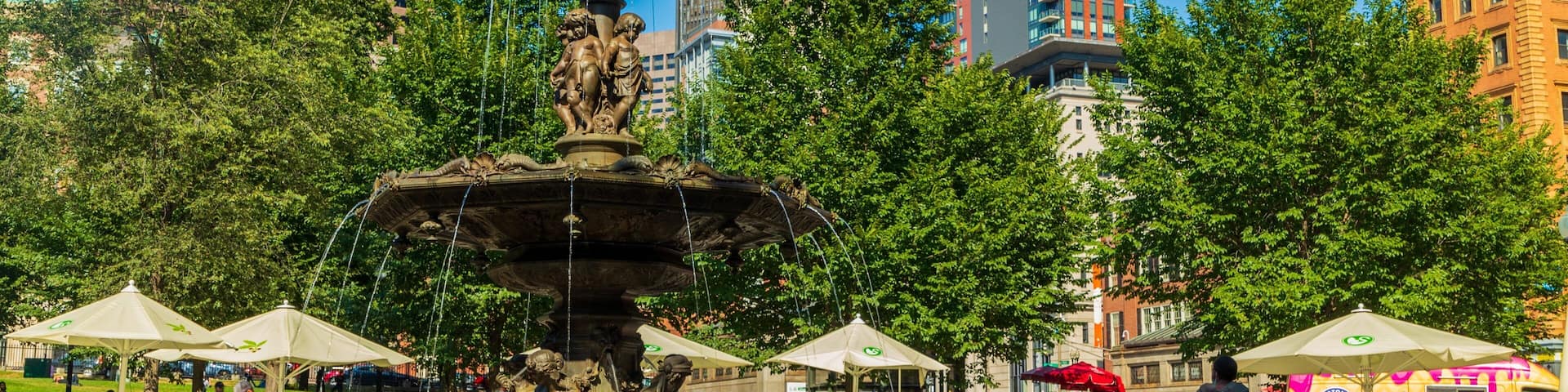 Un parque público con una gran fuente, rodeado de árboles y edificios modernos.