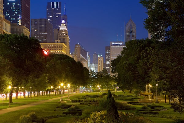 Un parc urbain de nuit, avec des pelouses bien entretenues, des arbres et une vue lointaine sur les gratte-ciel.