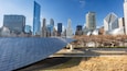 A modern cityscape with a distinctive metallic sculpture in the foreground and a variety of skyscrapers in the background.