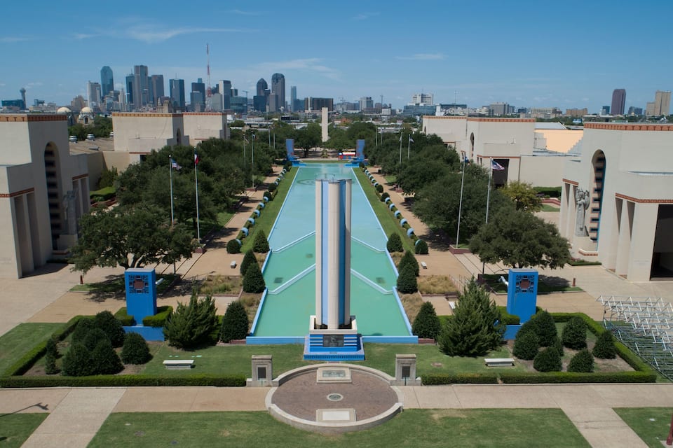 A cityscape with a central green pathway flanked by buildings and trees.