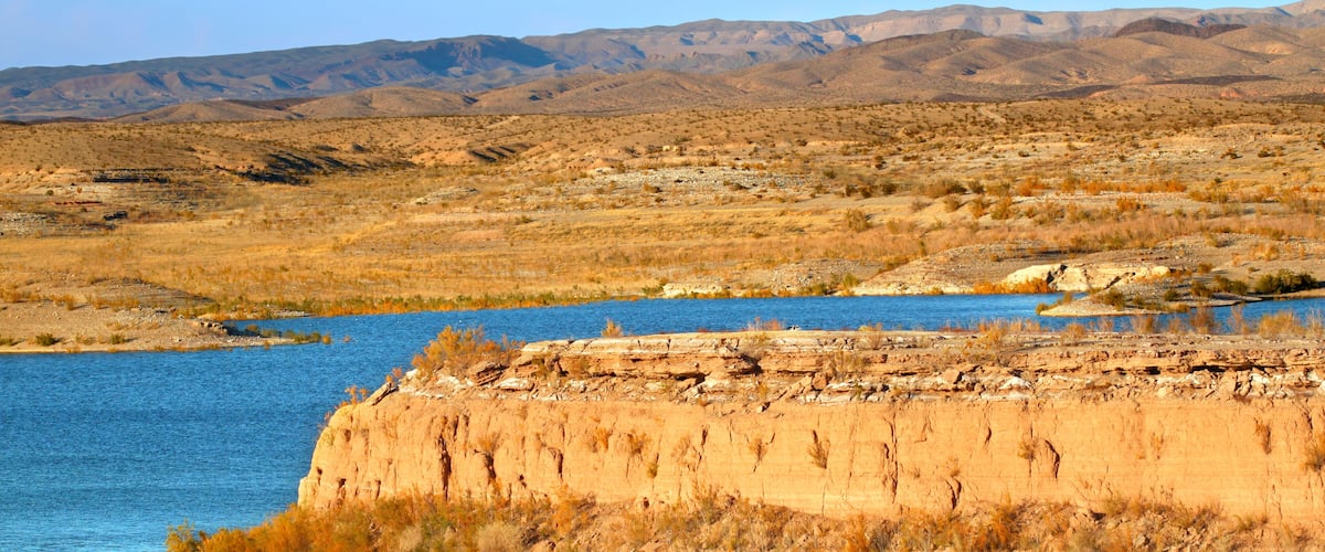 A river with a rocky cliff in the foreground and a dry, hilly landscape in the background.