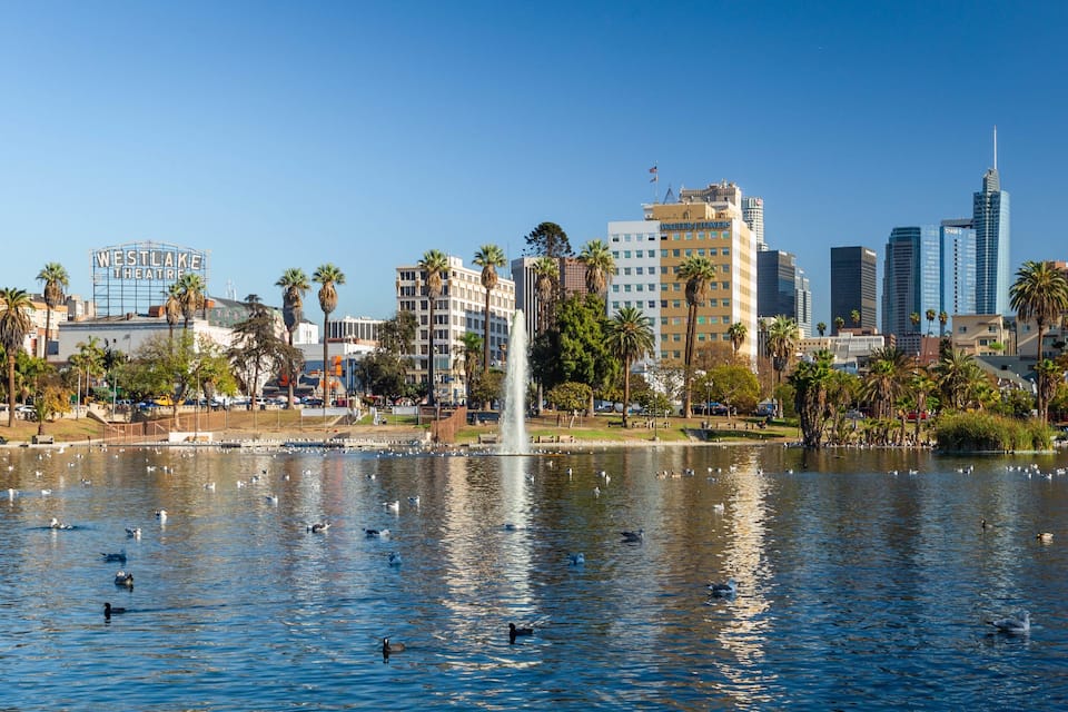 A cityscape with a large fountain, palm trees, and modern buildings including a skyscraper.