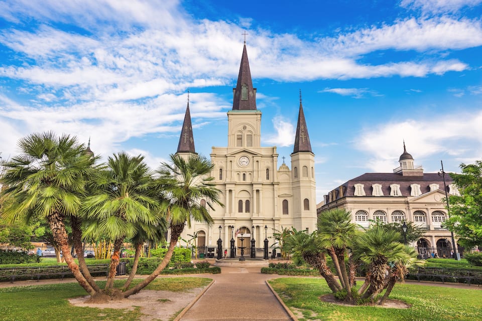 A large church with three spires and a dome, surrounded by palm trees and a pathway.