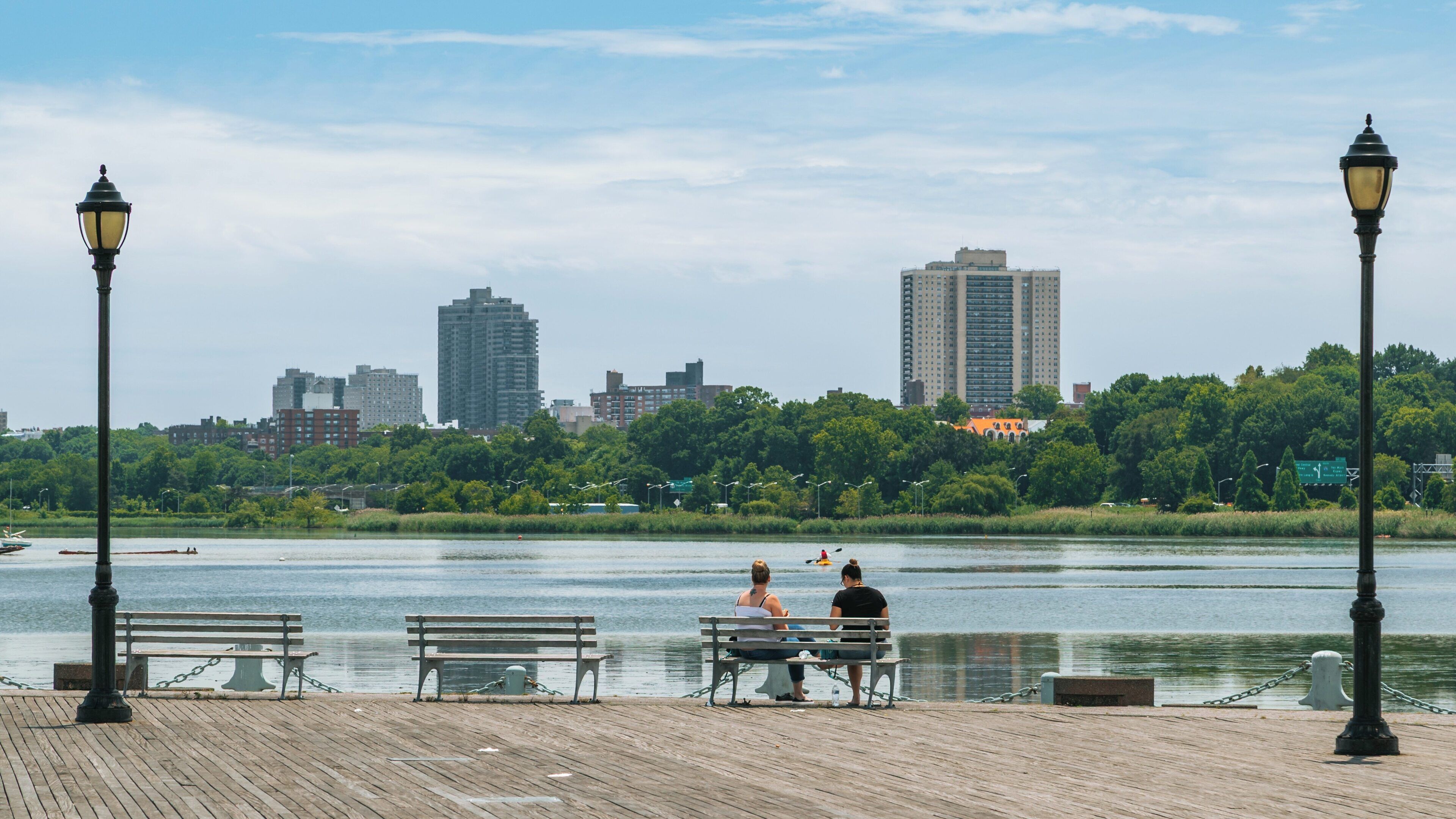 Visitors enjoy a sunny day by the water at Flushing Meadows-Corona Park in Queens, New York, showcasing the beauty of nature and urban life