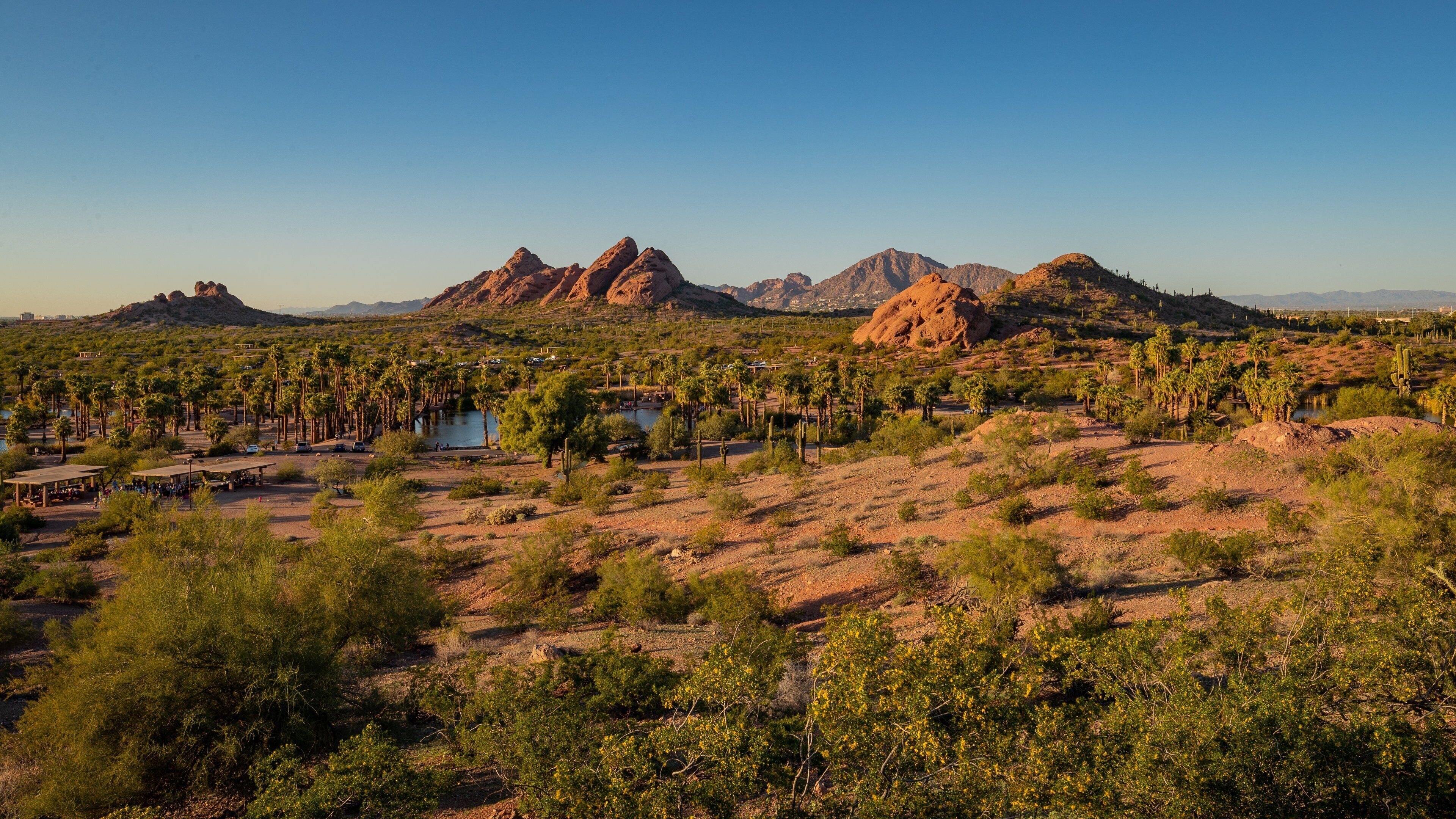 A desert landscape with rocky mountains, palm trees, and a small lake.