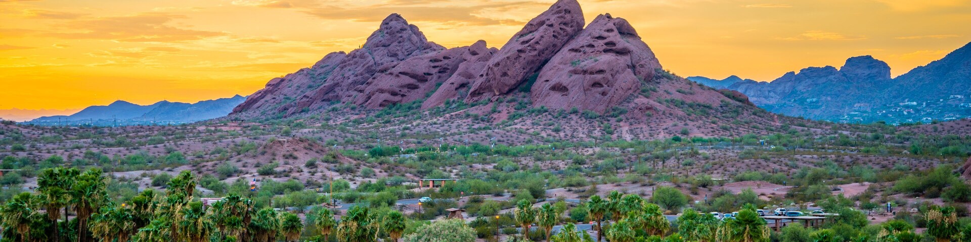 A desert landscape with prominent rock formations, palm trees, and a body of water.