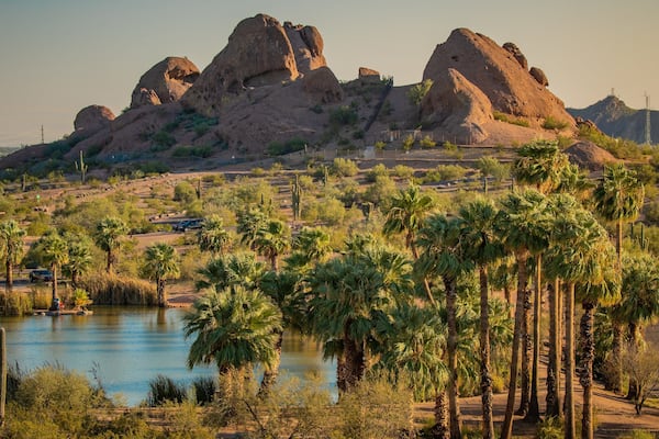 A desert landscape with a body of water, palm trees, and rocky formations.