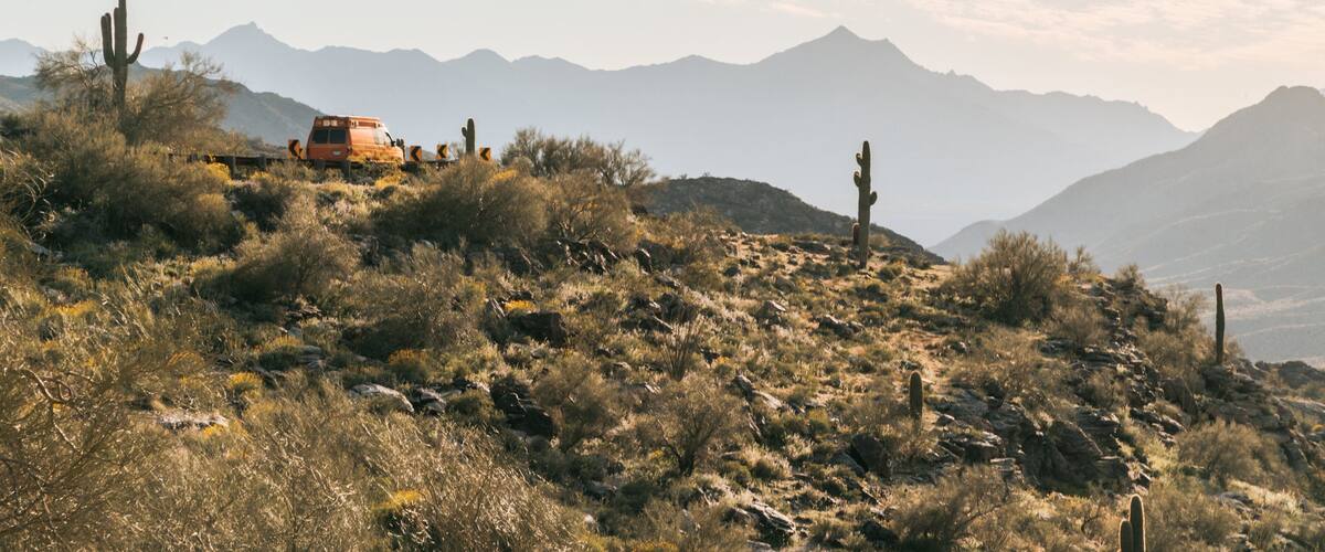 A desert landscape with cacti, a vehicle, and distant mountains.