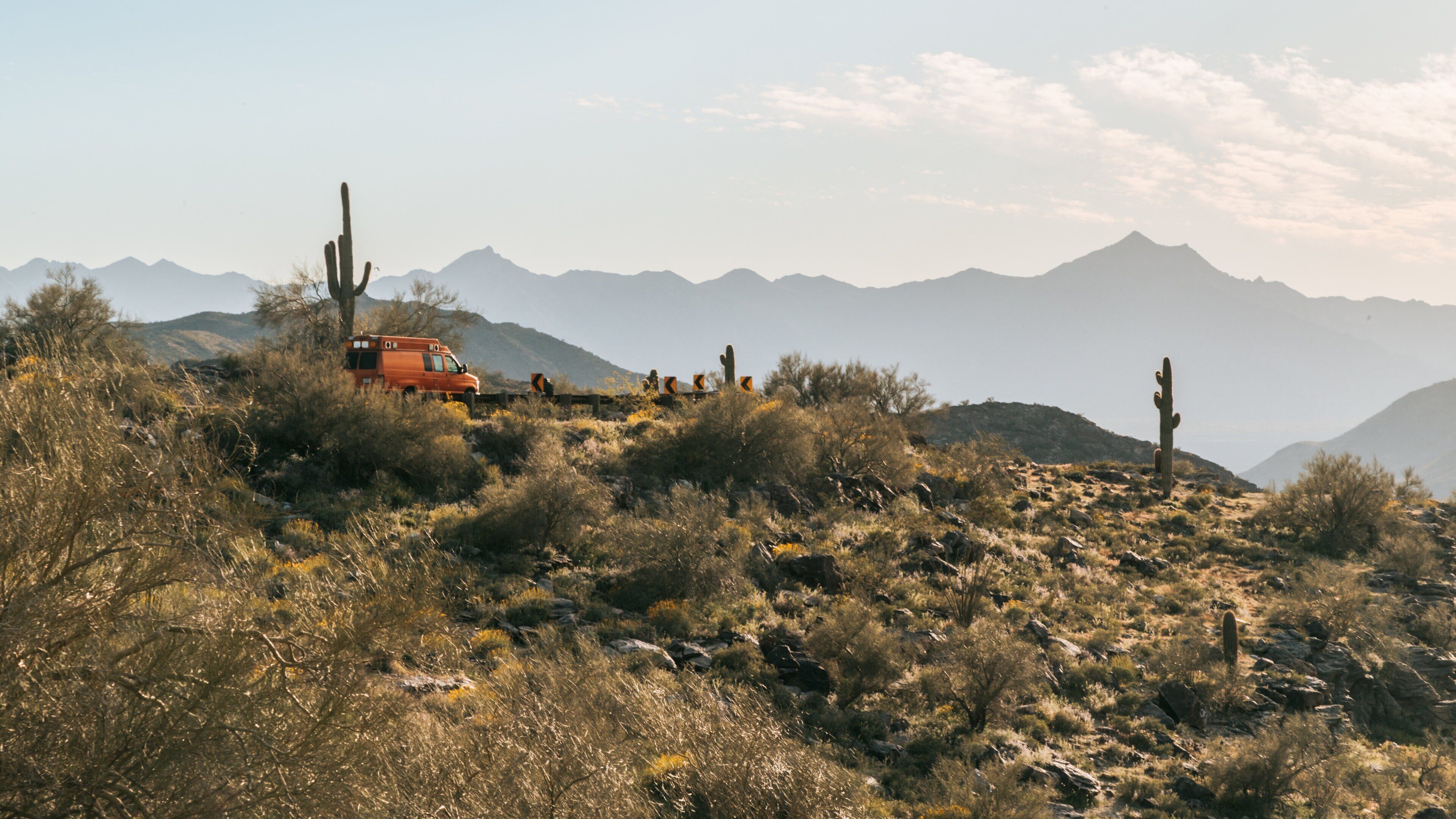 A desert landscape with a red vehicle, cacti, and distant mountains.