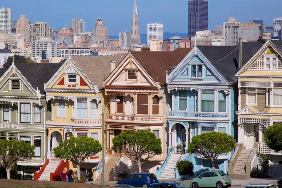 Una hilera de casas victorianas coloridas con un horizonte urbano al fondo.