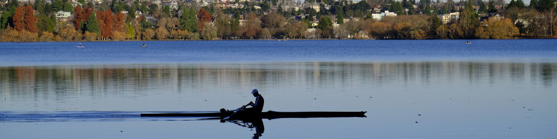 A calm lake with a rowboat and a distant shoreline with trees and buildings.