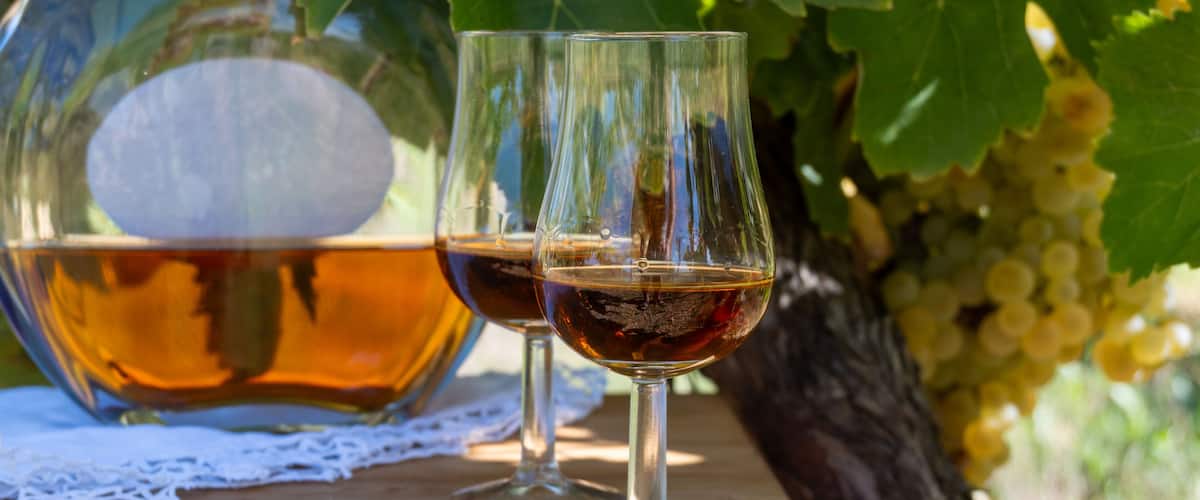 Two wine glasses on a wooden table with a bottle of wine and a lace doily.