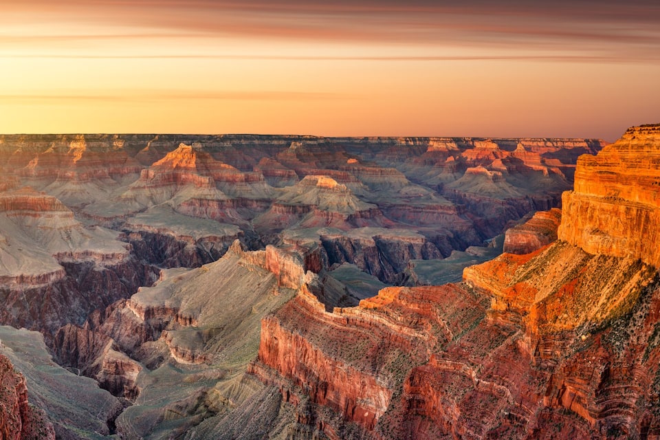 A vast canyon with layered rock formations and a sunset sky.