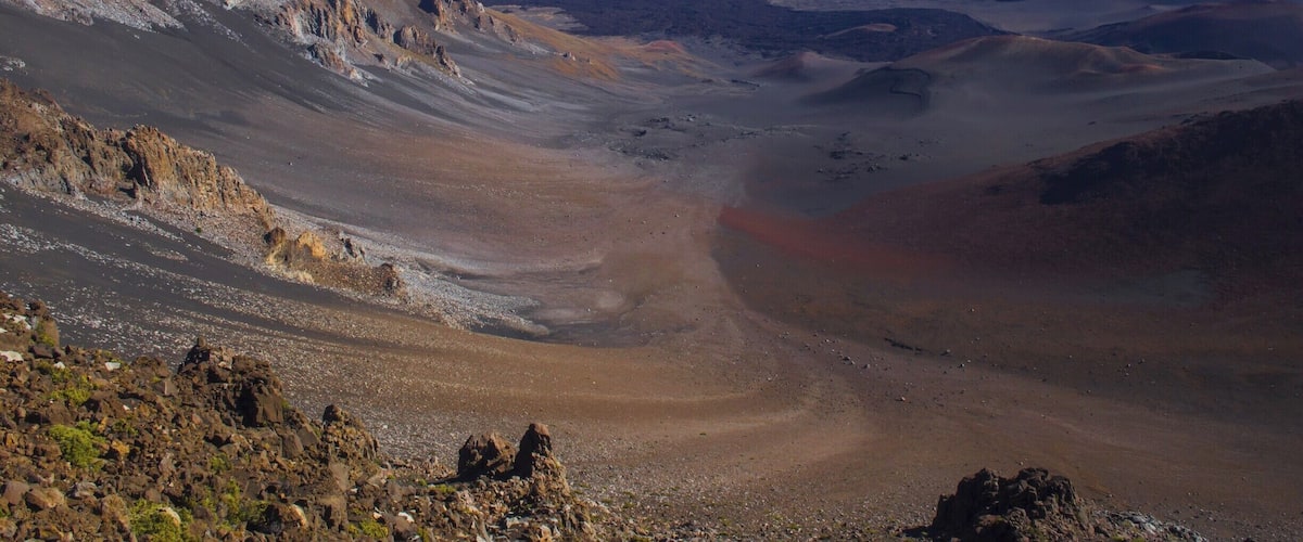 A barren volcanic landscape with rugged terrain and distant mountains.
