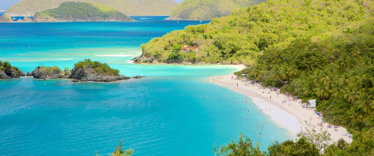 A tropical beach with clear turquoise waters, a sandy shore, and lush green hills in the background.