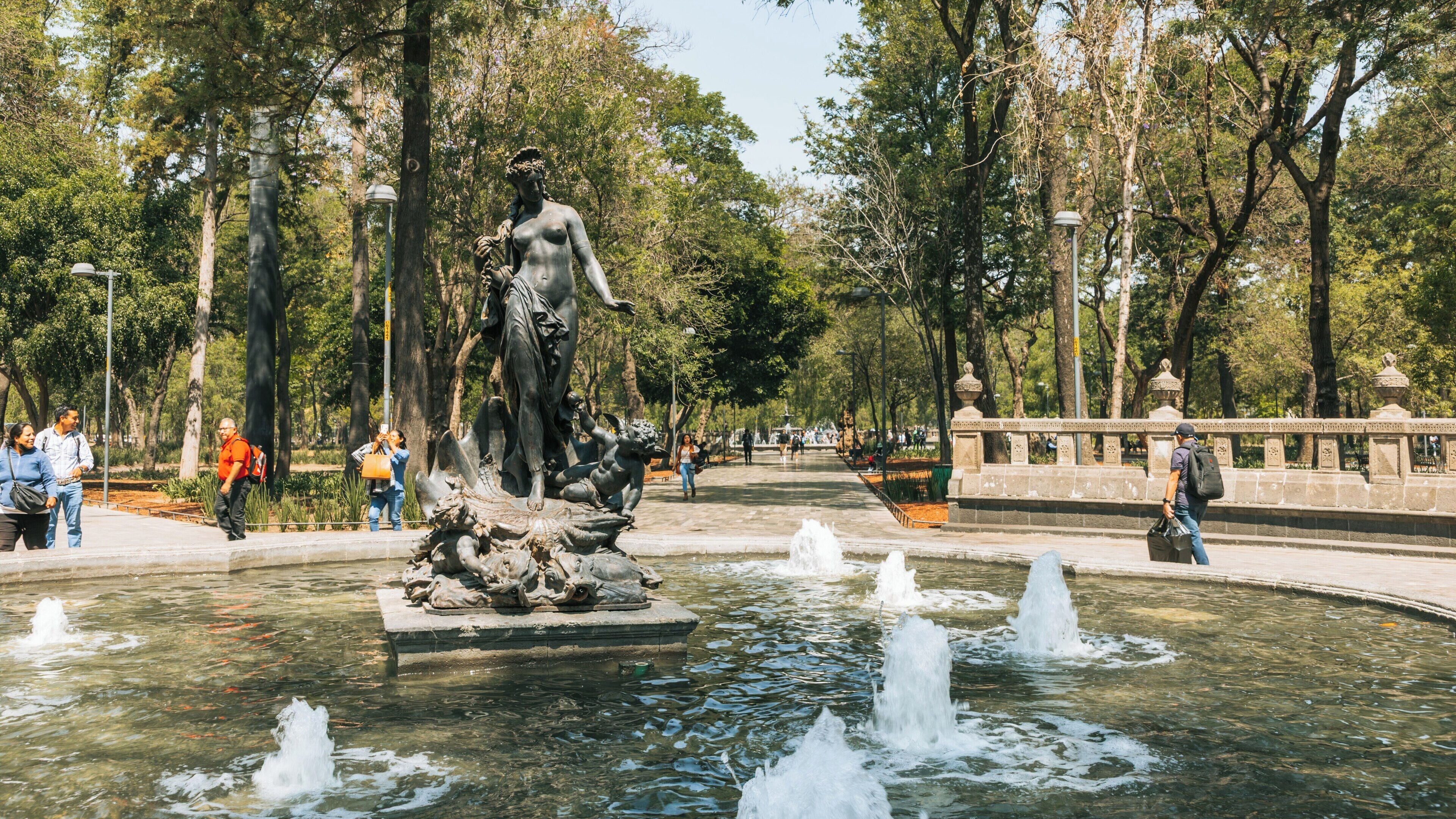 Visitors enjoying a sunny day at Alameda Central park in Cuauhtémoc, Mexico City, featuring a beautiful fountain and lush greenery