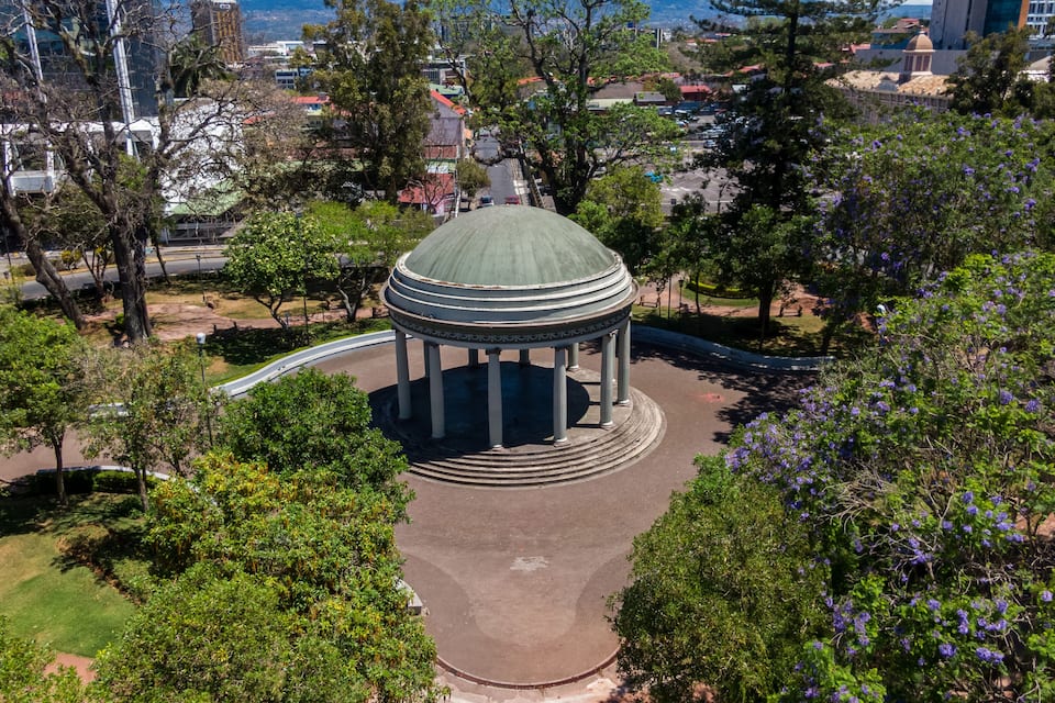 A gazebo with a dome roof surrounded by trees and a park.