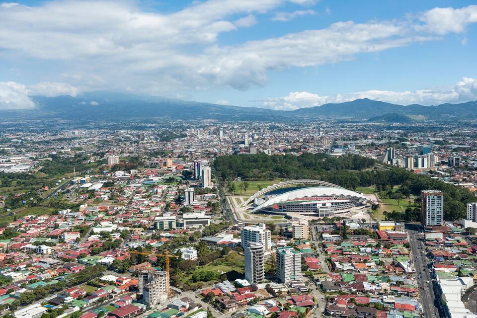 A cityscape with a stadium, residential areas, and mountains in the background.