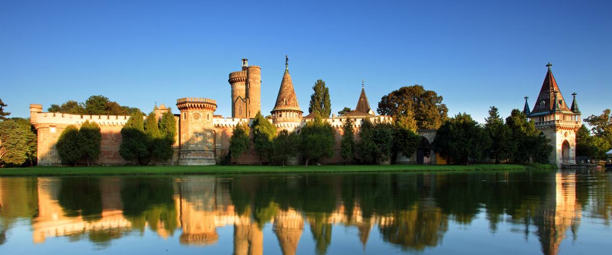 A castle with multiple towers and a moat reflecting the structure.