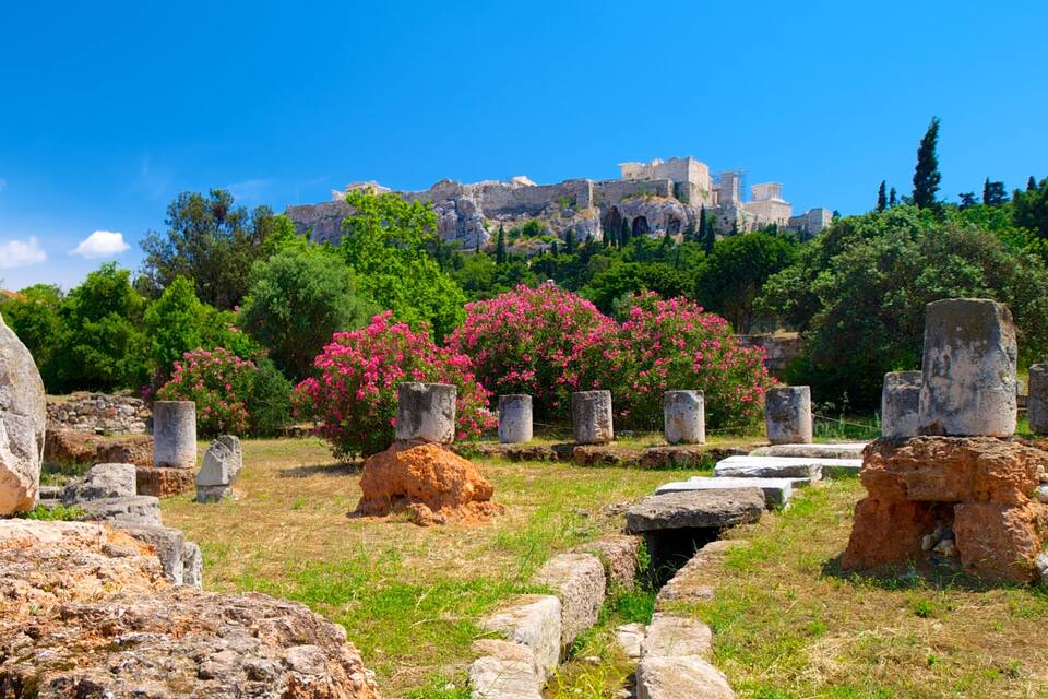 Ancient ruins with stone columns and a backdrop of a historic building.