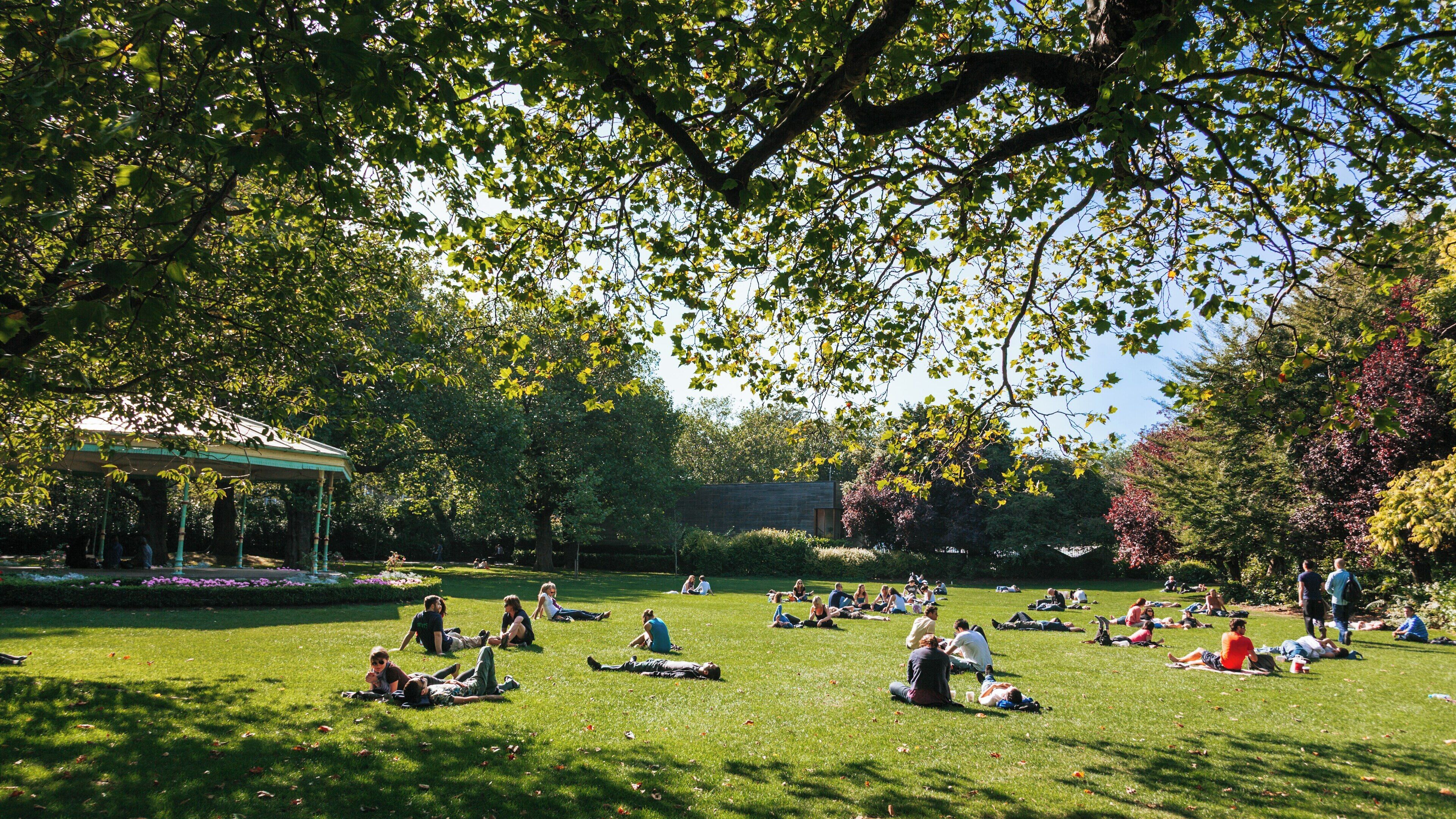 Visitors enjoy a sunny day on the grass at St. Stephen's Green park in Dublin, Ireland amidst vibrant greenery and cheerful atmosphere