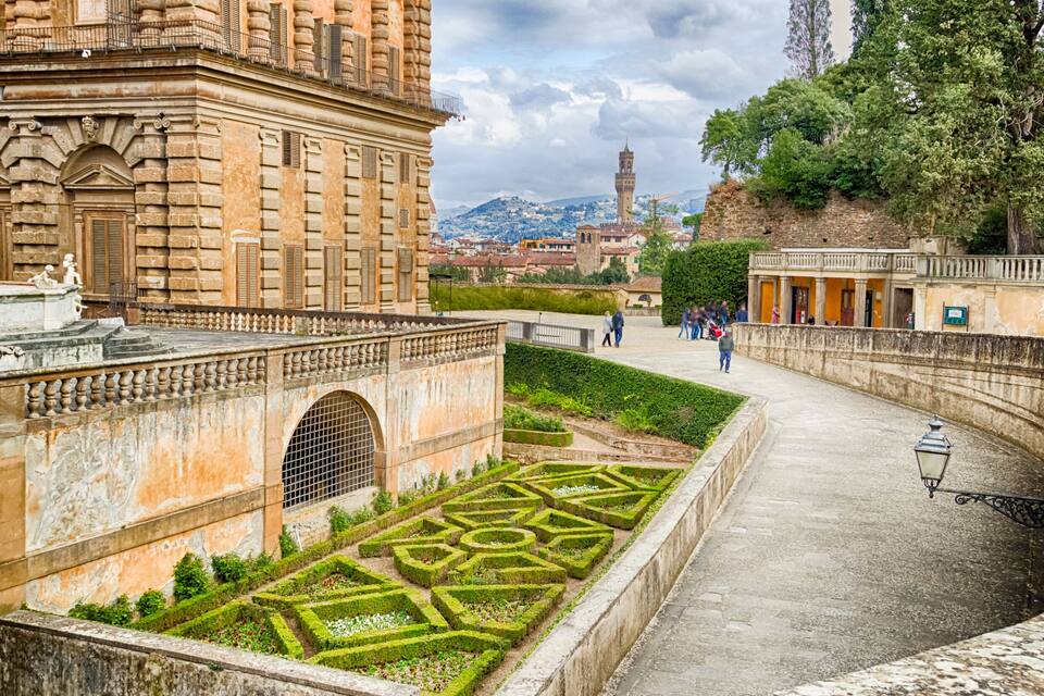 Edifici històric amb un laberint de jardí, una torre al fons i un passeig pavimentat.