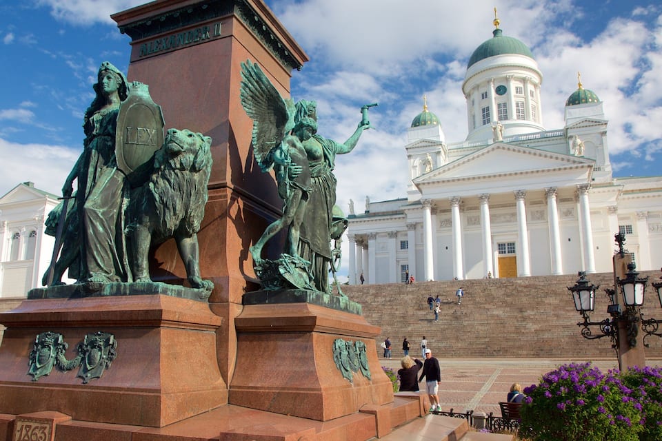 A bronze statue of a historical figure, a large white building with domes, and a clear blue sky.