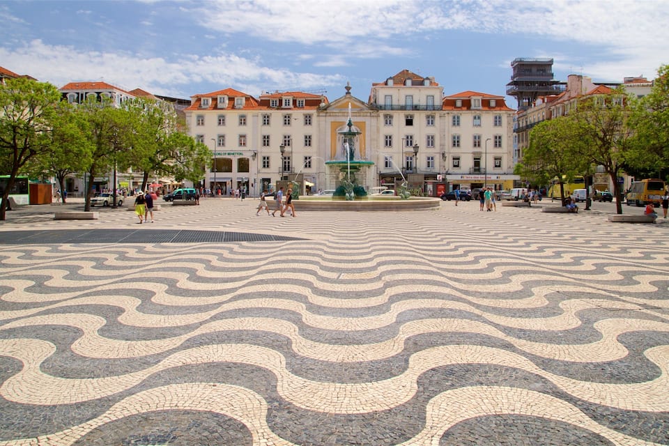A plaza with patterned pavement, a fountain, and historic buildings in the background.