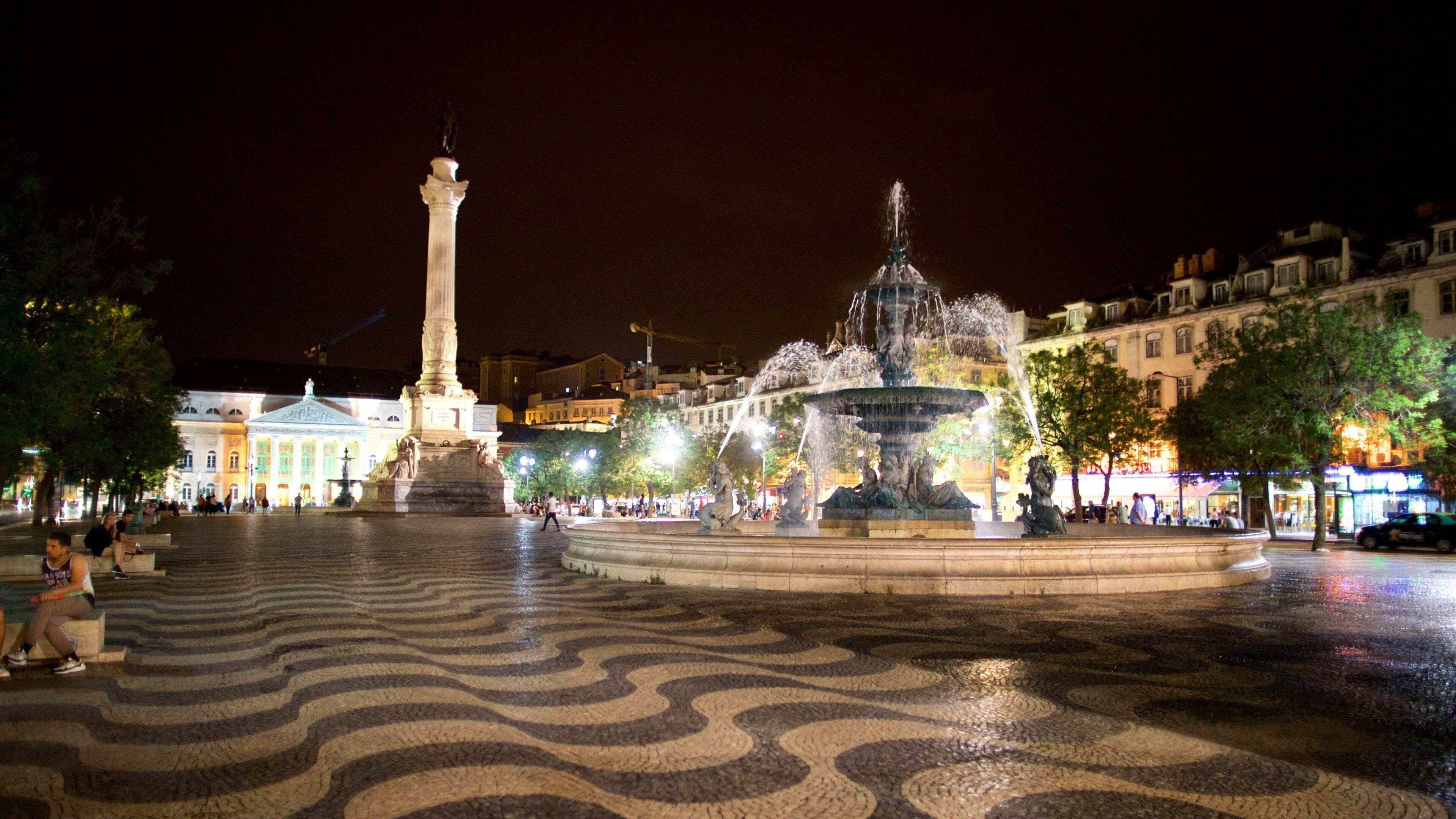 Une place agrémentée d’une fontaine, d’un monument et d’un pavage décoratif.