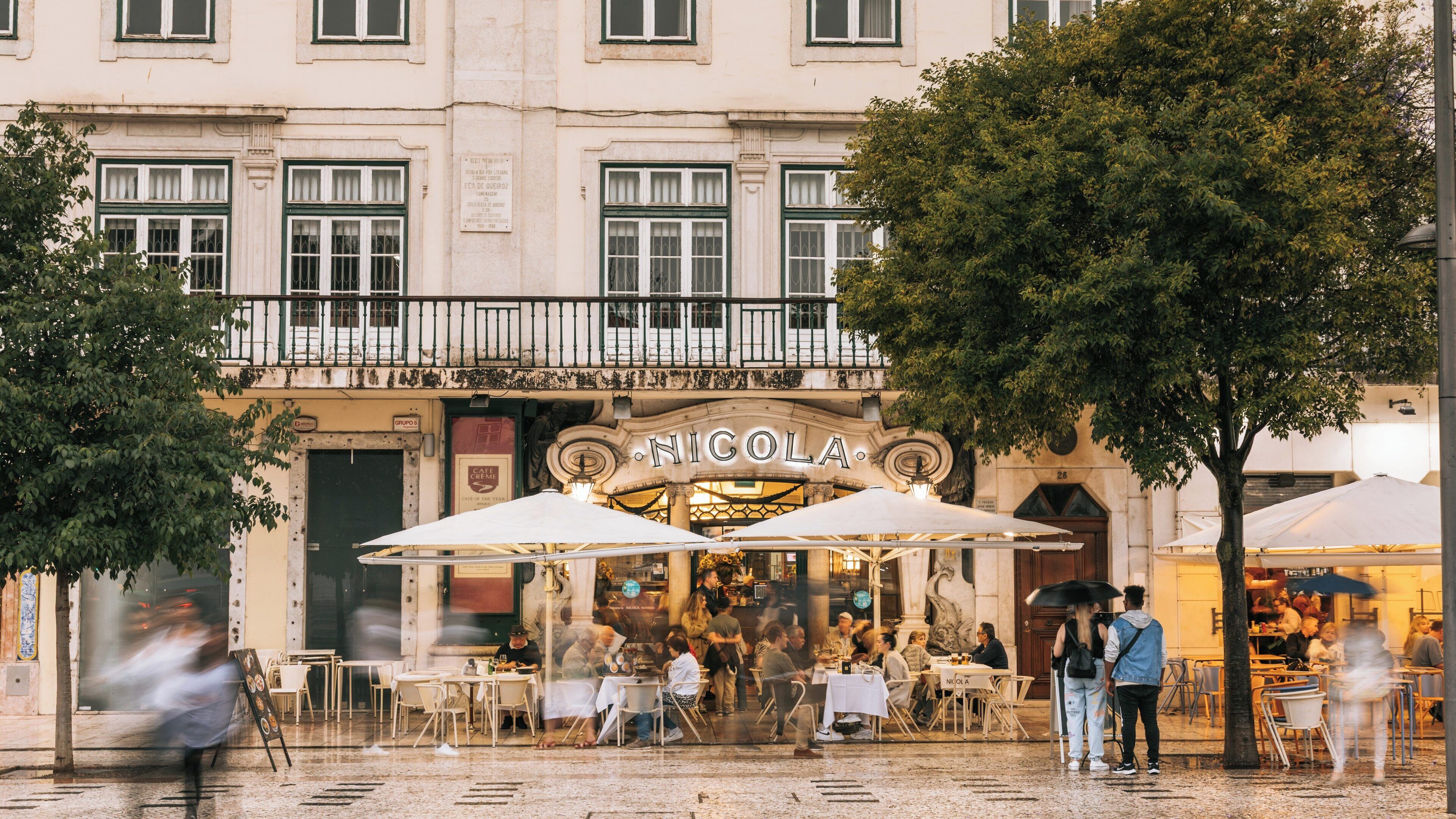 People sit at tables outside the Nicola cafe in rossio square, baixa district, lisbon, portugal, on a rainy day, creating a vibrant and bustling atmosphere