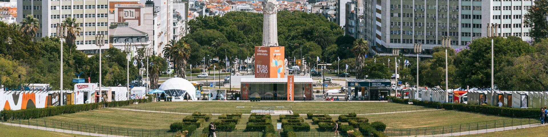 Un paisaje urbano con un monumento central, un parque amplio y abierto con setos podados, y una masa de agua al fondo.