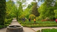 A lush garden with a central pathway, manicured hedges, and a stone fountain.
