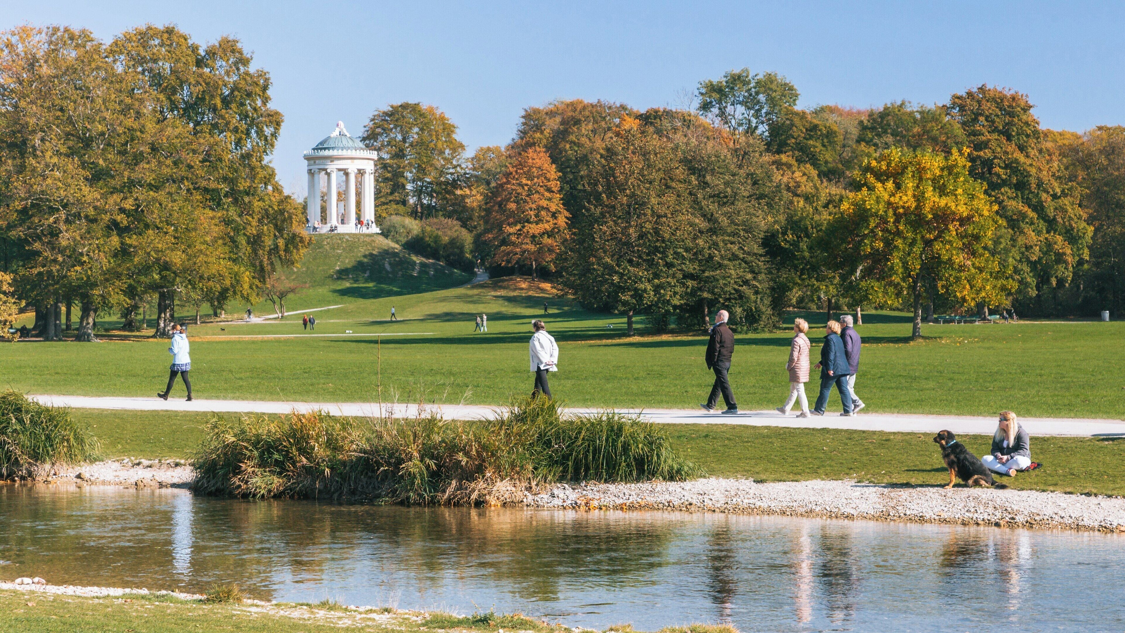 People enjoy a sunny day at English Garden in Munich, exploring trails and relaxing by the river in autumn
