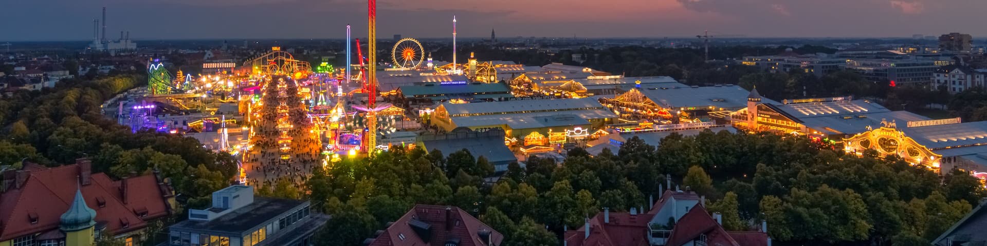 Un paisaje urbano al anochecer con atracciones de parque de diversiones iluminadas y una noria.