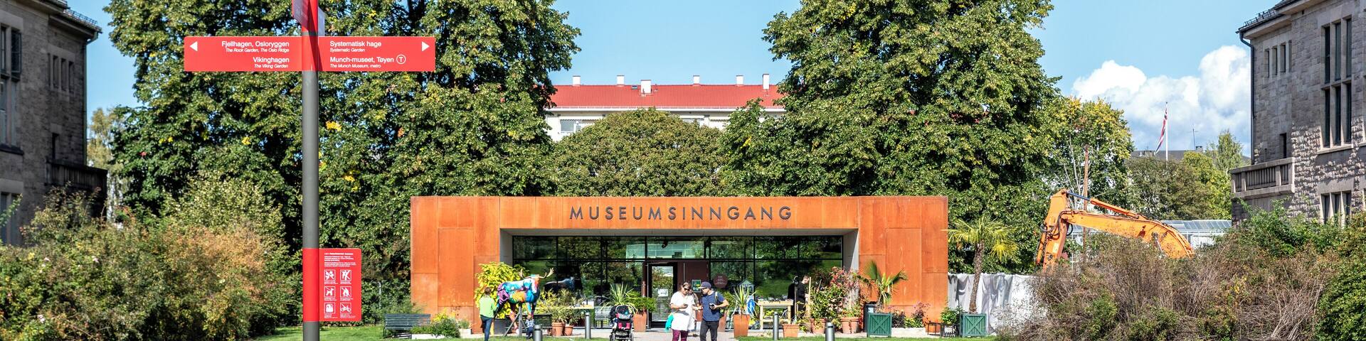 A pathway leading to a museum entrance with directional signs, surrounded by greenery and trees.