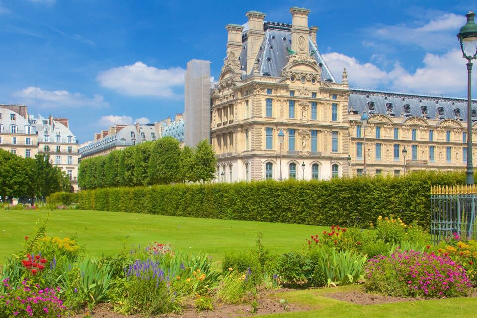 A historic building with ornate architecture, a well-maintained lawn, and a variety of colorful flowers.
