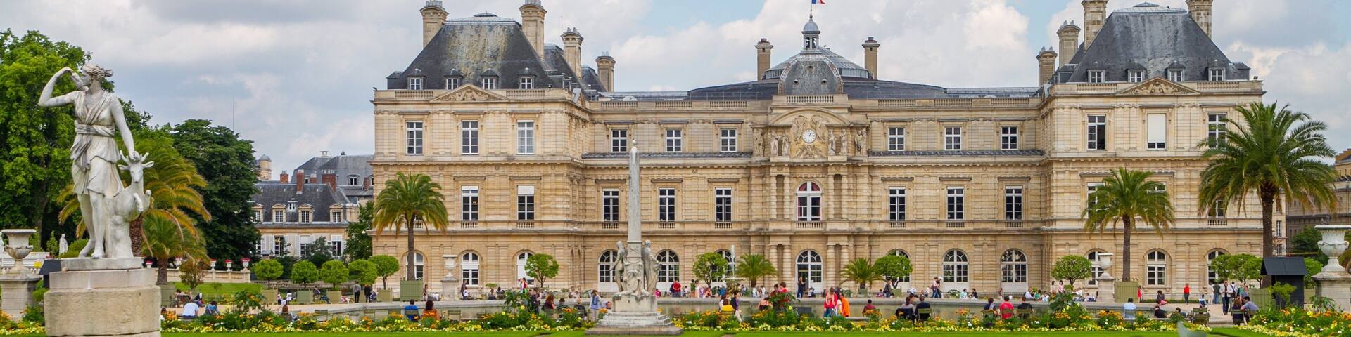 A large historic building with a well-manicured lawn and statues.