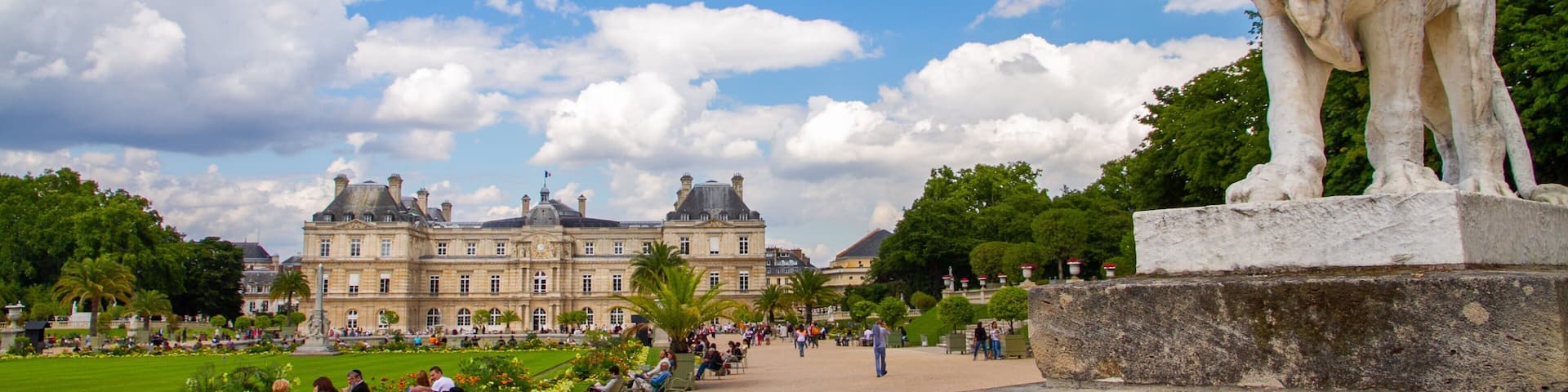 A large stone lion statue in a park with a historic building in the background.