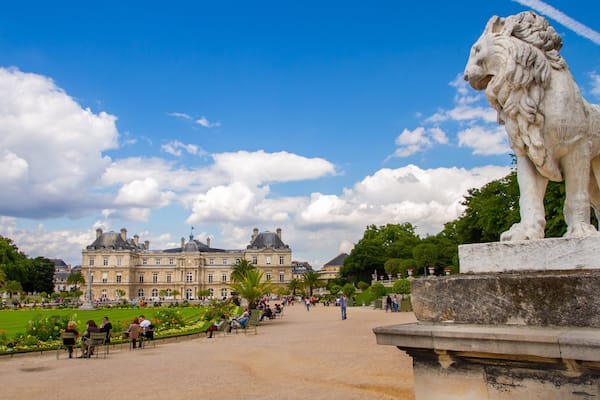 Une grande statue de lion en pierre, dans un parc, avec un bâtiment historique en arrière-plan.
