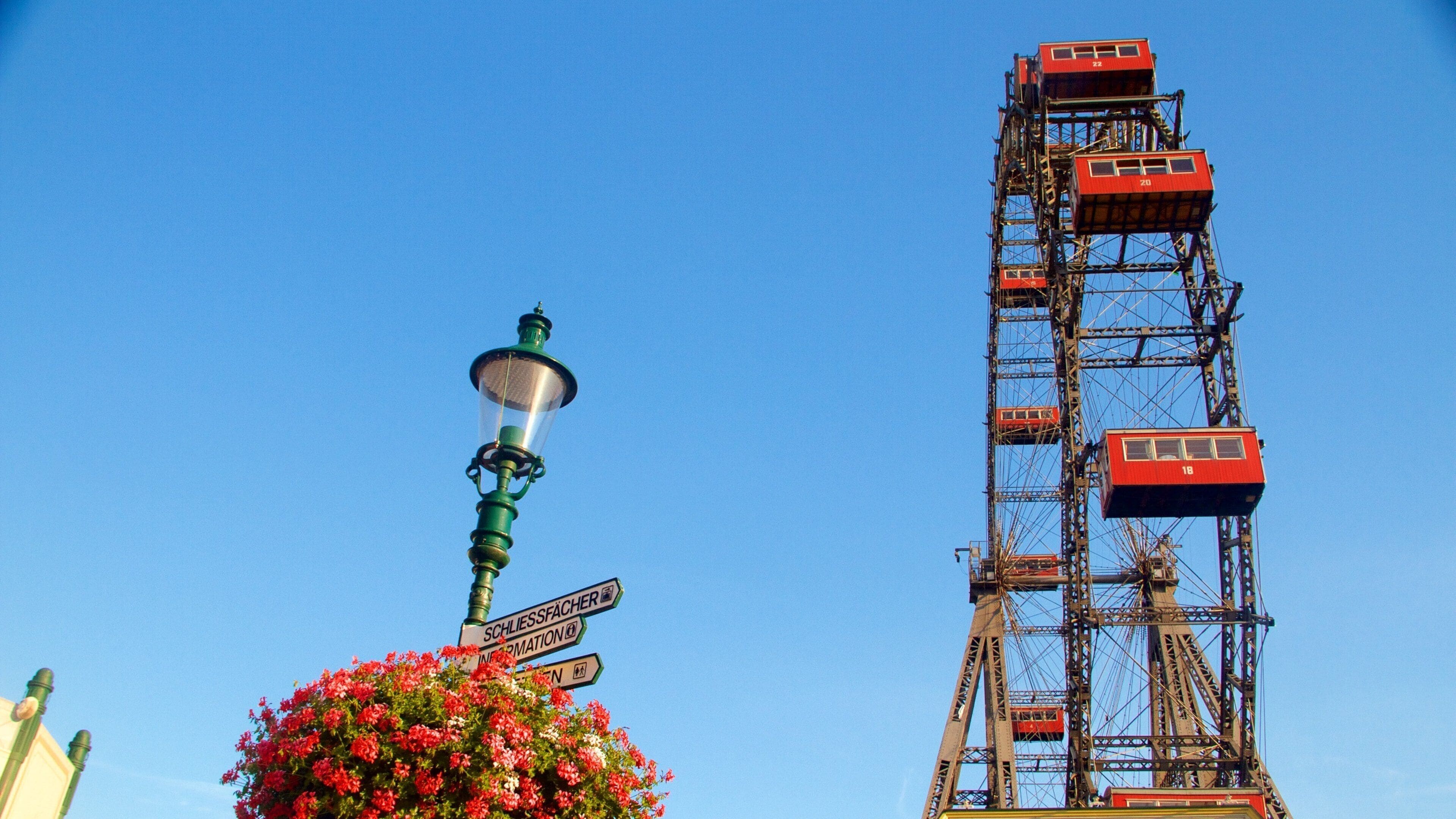 Una farola con señales de dirección y la torre roja de un teleférico.