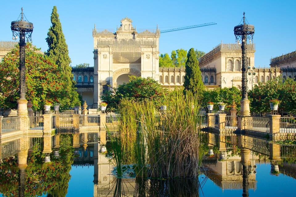 Um edifício histórico com arquitetura elaborada, um corpo d'água reflexivo e postes de luz decorativos.